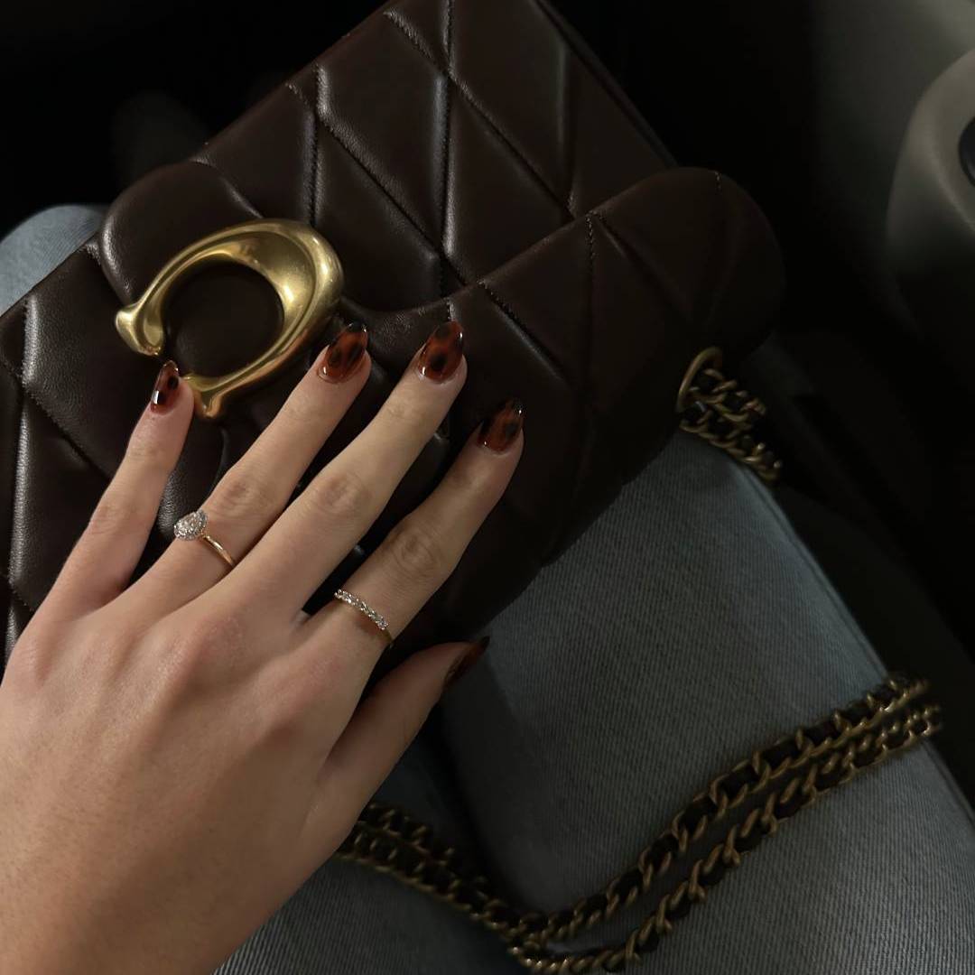 hand with burgundy nail polish resting on a leather purse